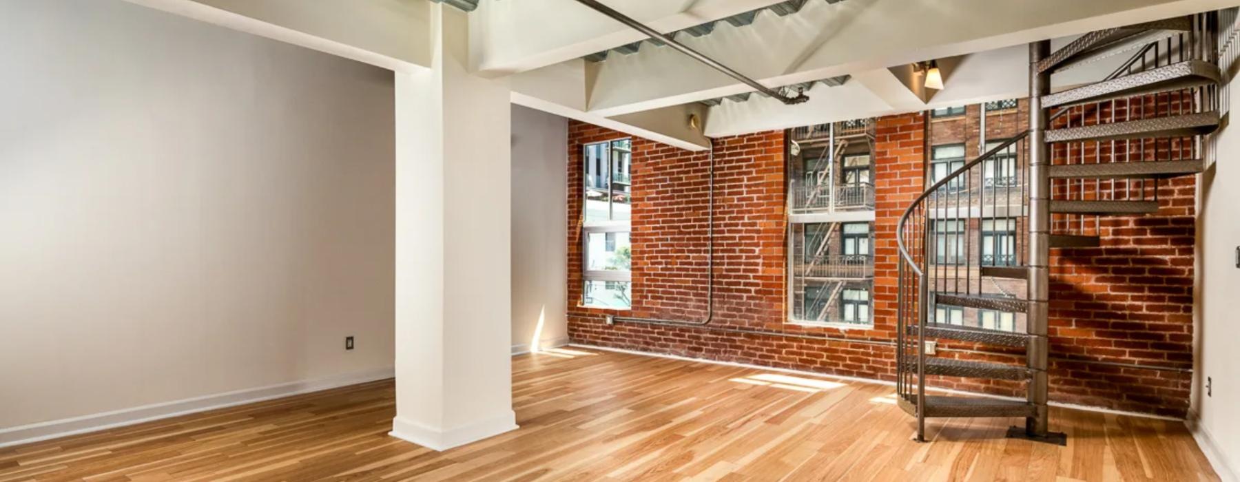 a room with a wood floor, brick walls, and windows